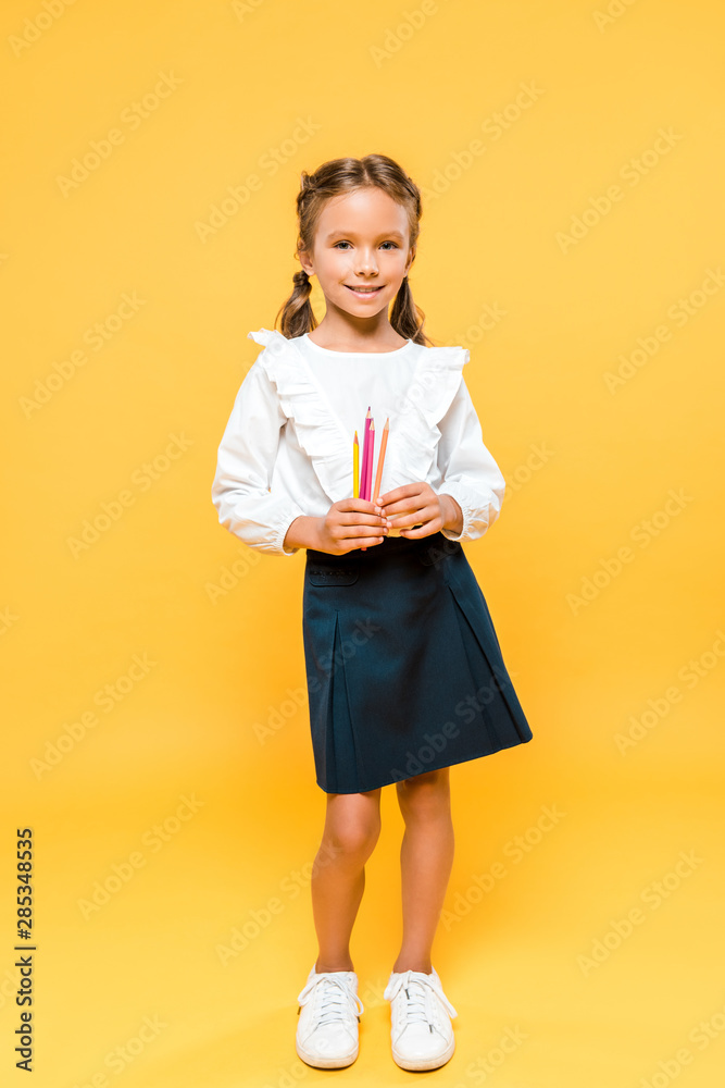 Fototapeta premium happy schoolkid holding color pencils on orange