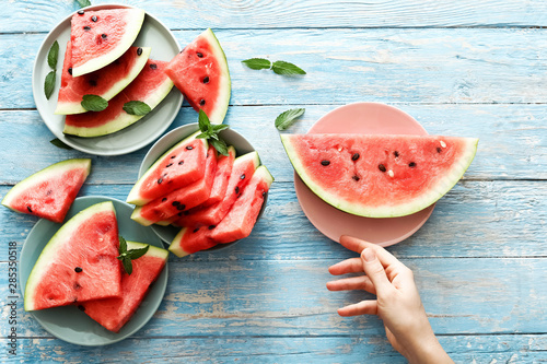 Fresh red watermelon slice, female hand on an blue rustic wood background with copy space.  Top view. Summertime concept.