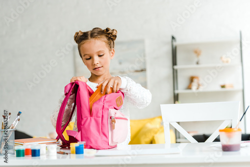cute schoolgirl putting lunch box in pink backpack