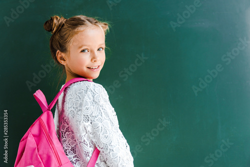 happy schoolkid smiling while standing with backpack on green