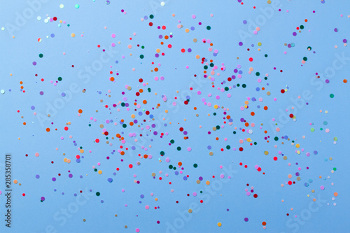 Multicolored round sequins on a pastel blue background with confetti.
