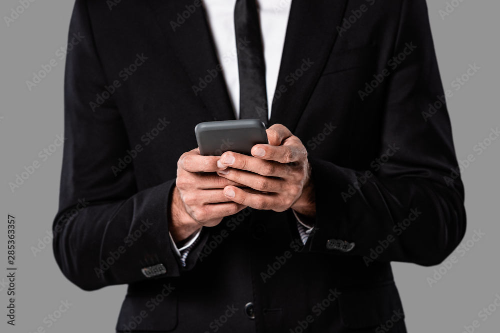 partial view of businessman in black suit using smartphone isolated on grey partial view of businessman in black suit using smartphone isolated on grey