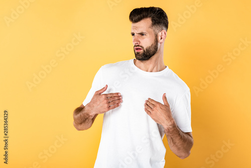 indignant handsome man in white t-shirt isolated on yellow photo