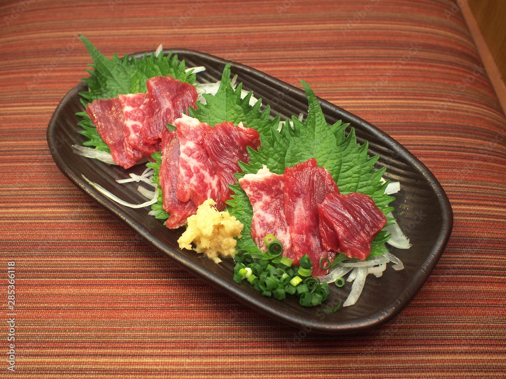 Raw Horse meat sashimi on blace ceramic plate served with ginger and onions