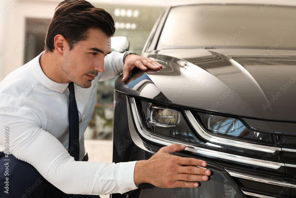 Young man checking new car in modern dealership