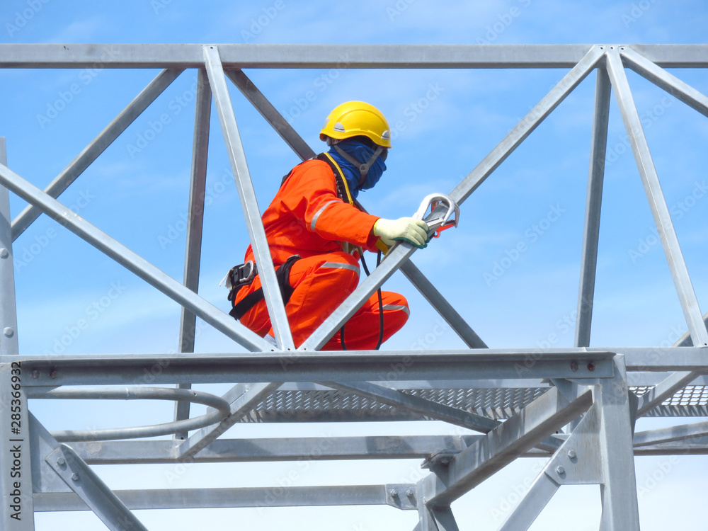 Man Working on the Working at height. Professional industrial climber in helmet and uniform works at height. Risky extreme job. Industrial climbing at construction site. Man Working on the Working at height. Professional industrial climber in helmet and uniform works at height. Risky extreme job. Industrial climbing at construction site.