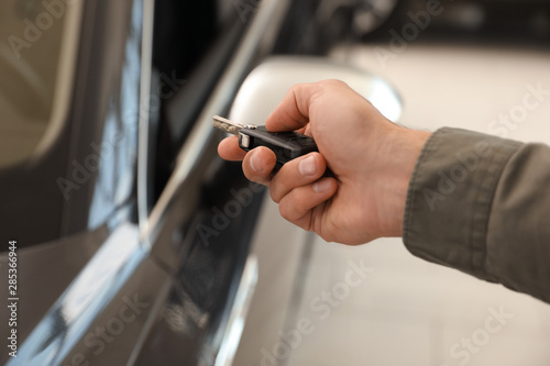 Young man checking alarm system with car key indoors, closeup