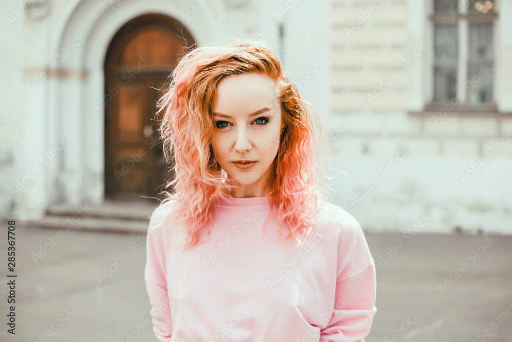 Fototapeta premium Young brunette girl in black standing outside and watching the sunset in the city, the sun shines brightly, fashionable clothes on a girl, hipster style,, tattoo, street, freedom, pink color, moodl