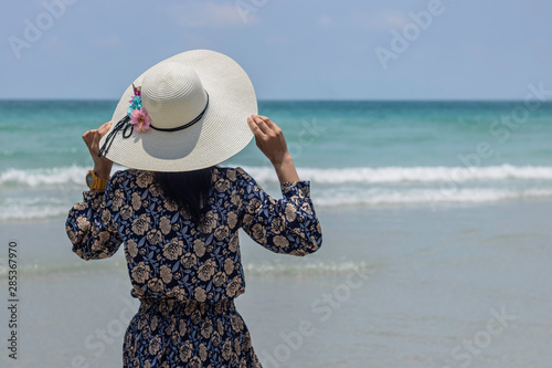 Stand up the rear view of the girl wearing a hat to relax outside the beach and look at the sea view at Sattaheeb, Thailand. photo