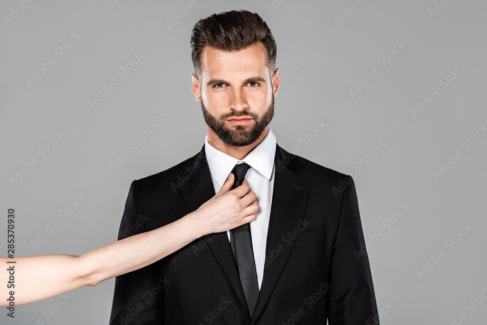 woman touching tie on handsome businessman in black suit isolated on grey woman touching tie on handsome businessman in black suit isolated on grey