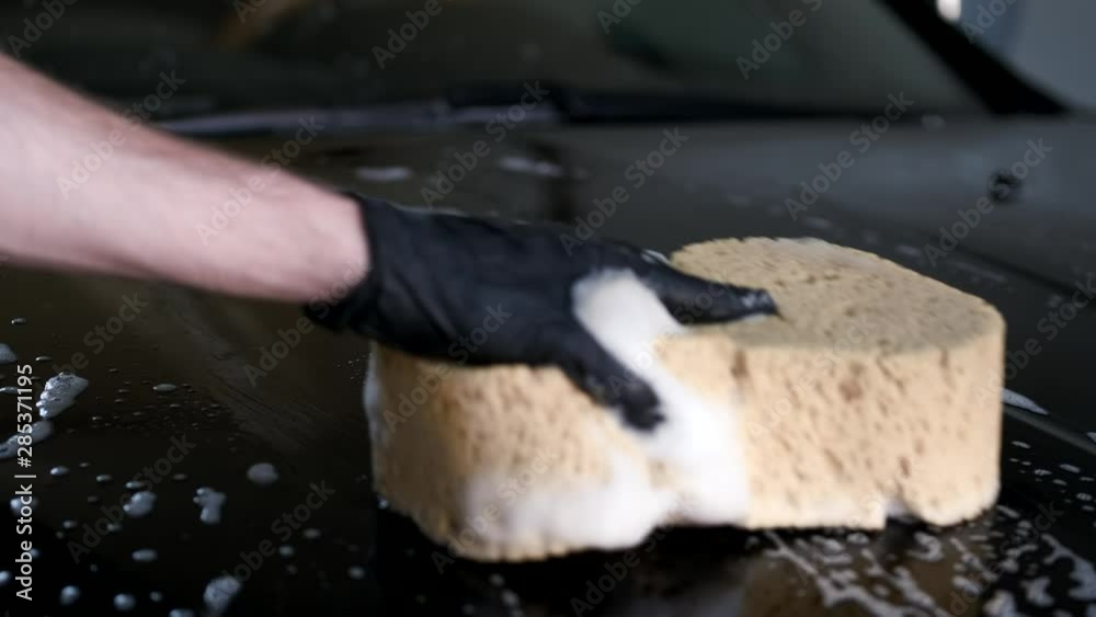 Man in a garage. Worker washing a car. Sponge in a hand Man in a garage. Worker washing a car. Sponge in a hand