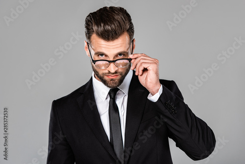 confident successful businessman in black suit and glasses isolated on grey