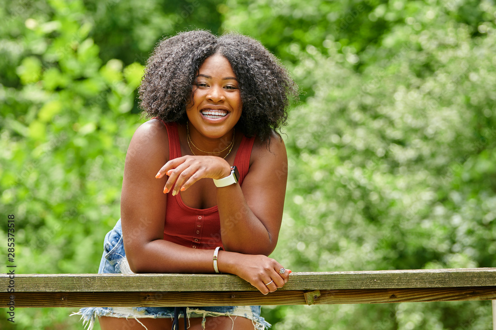 Naklejka premium Beautiful African-American female model smiles as she poses in orange tank top in woods