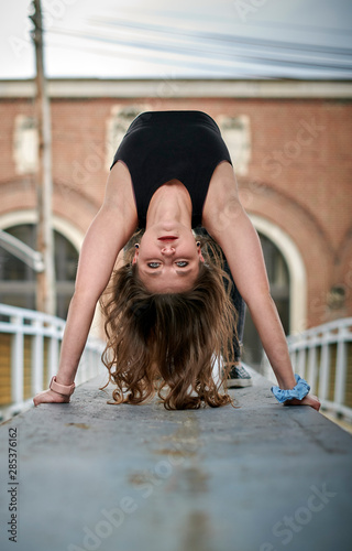 Beautiful young woman poses in athletic wear in urban setting - gymnastics or cheer - doing back walkover towards camera
