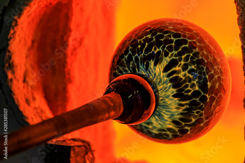 Glass blower working on a bubble of melted glass on a rod by heating it up in a kiln at a glass maker's workshop