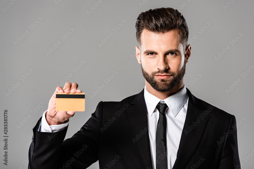 confident businessman in black suit holding credit card isolated on grey confident businessman in black suit holding credit card isolated on grey