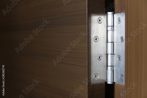Stainless door hinges on dark wooden swing door for interior design. Horizontal shot.