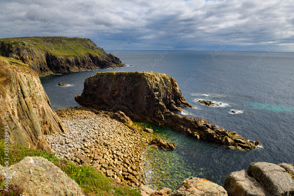 Granite cliff with shoreline boulders at Enys Dodnan rock arch and Pordenack Point at Land's End Cornwall England Granite cliff with shoreline boulders at Enys Dodnan rock arch and Pordenack Point at Land's End Cornwall England