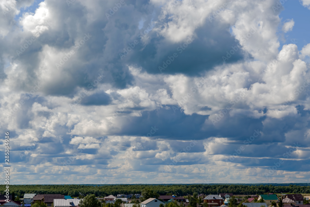 Gray with white storm clouds in the sky over the roofs of houses in the city, beautiful summer landscape, background