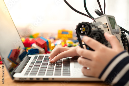 Closeup : hands of preteen / teenage boy codes blocks Mindstorms on his computer laptop, other hand holds robot build for school project. STEM Education, Programming, Robotic Technology, Online Learning photo