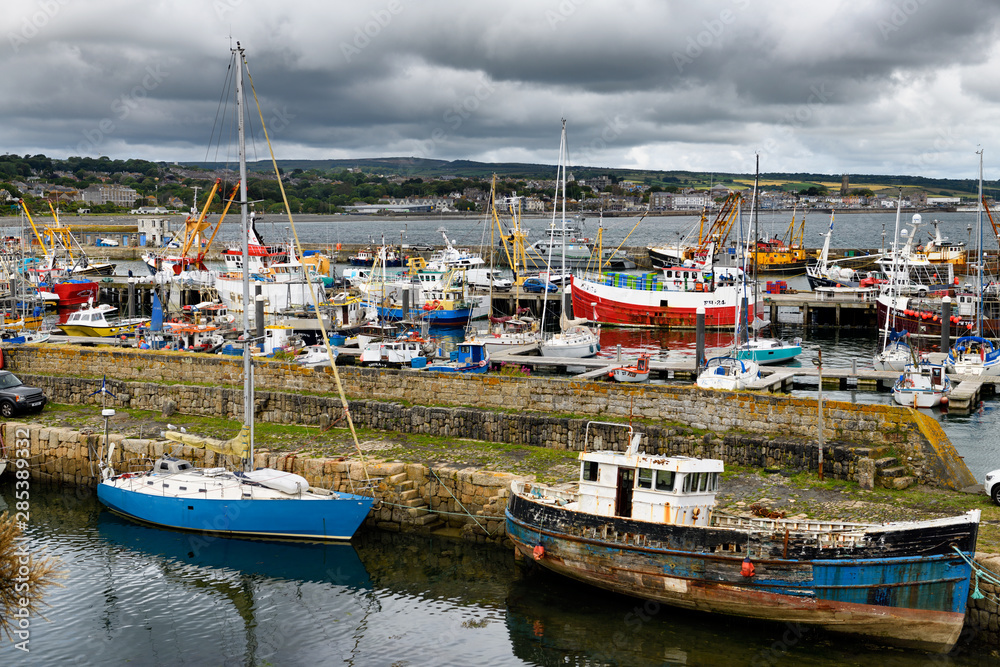 View of various boats moored at stone piers of Newlyn harbour with view of Penzance across Mounts Bay Cornwall England