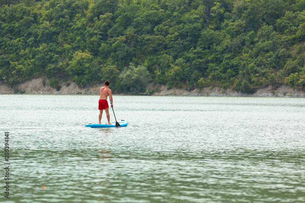 Naklejka premium A young guy is floating on a Board La sup surfing on the lake.