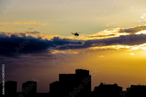 A helicopter flies over the city in the evening during sunset.