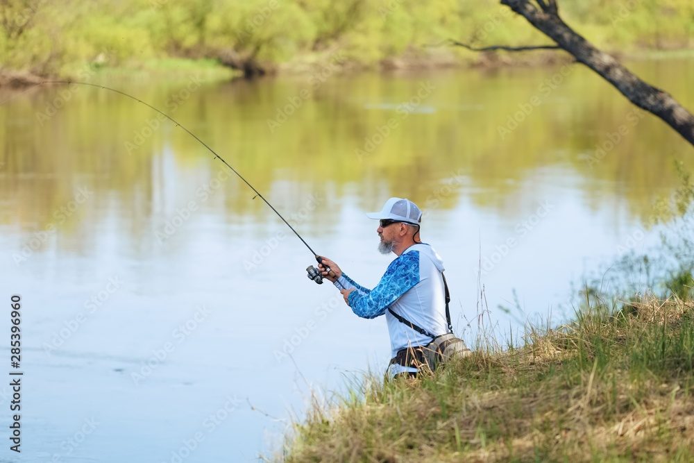 Man fish with spinning on river bank, casting lure. Outdoor weekend activity. Photo with shallow depth of field taken at wide open aperture. Man fish with spinning on river bank, casting lure. Outdoor weekend activity. Photo with shallow depth of field taken at wide open aperture.