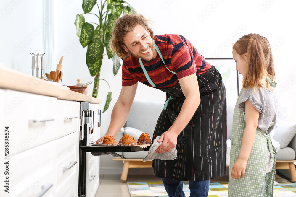 Obraz premium Young man and his little daughter baking tasty muffins at home