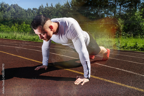 Young man in sportswear making pushups on a stadium