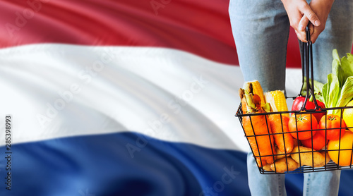 Photography Woman is holding supermarket basket, Netherlands waving flag background