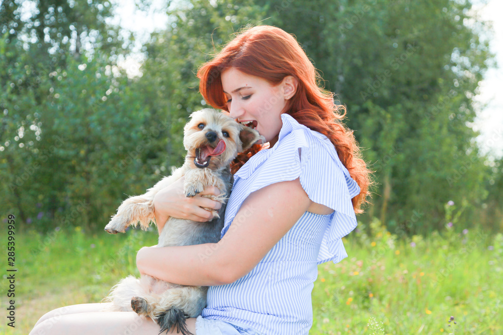 Cheerful pretty young woman sitting and hugging her dog on the nature