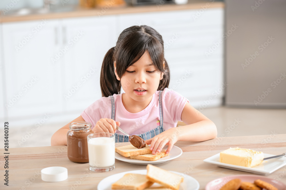 Funny little girl eating tasty toasts with chocolate spreading in kitchen Funny little girl eating tasty toasts with chocolate spreading in kitchen