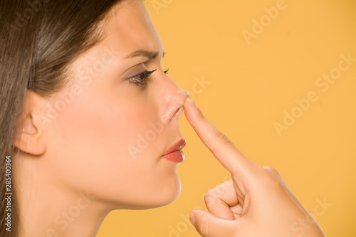 Beautiful young woman touching her nose with her finger on yellow background photo