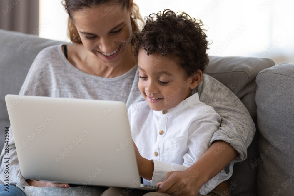 Happy mother embrace african cute kid son learning using laptop