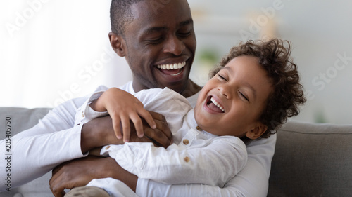 Happy black father tickling african kid son laughing cuddling together