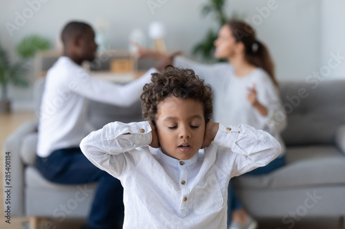 Upset african kid son closing ears not listening parents fighting