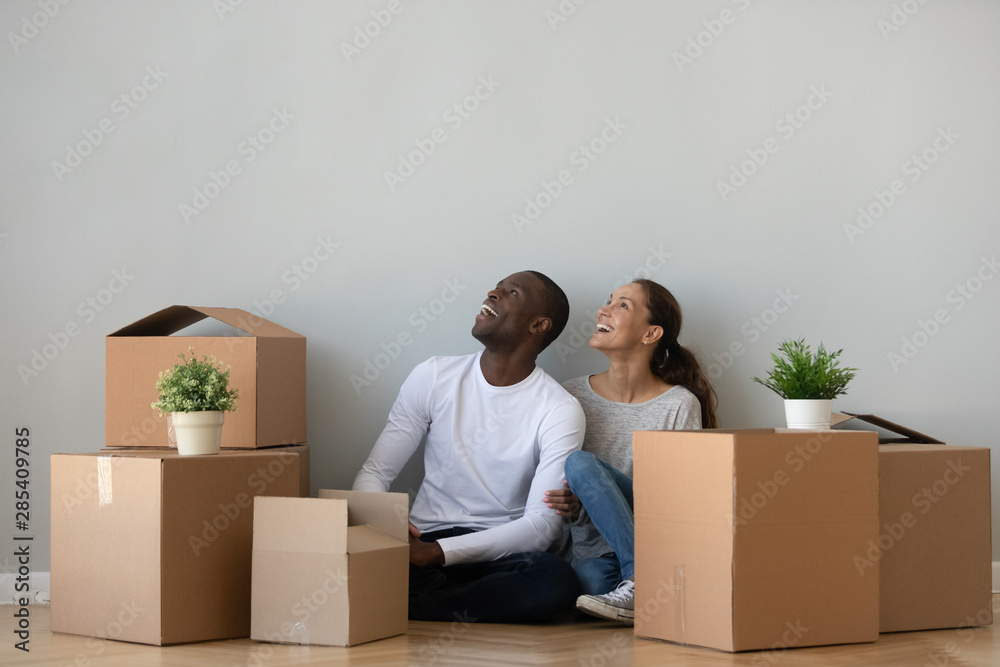 Excited mixed ethnicity couple dreaming in own home with boxes