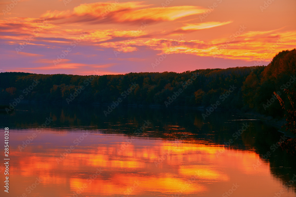 beautiful sunset in autumn season - trees silhouette near a river, bright sunlight