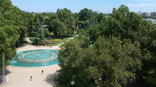 drone shot of giant fountain in a park on sunny summer day with people walking and relaxing.mp4