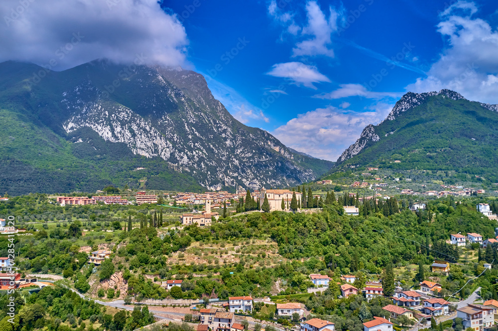 Obraz premium The resort town of Pulciano, located on the shores of Lake Garda. San Michele Arcangelo Church is located on a mountain. Panoramic view of the city, church, Lake Garda, Alps. Aerial view.
