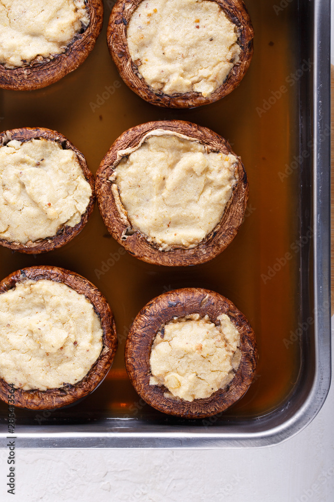 Baked stuffed champignon caps and baked cherry tomatoes on baking sheet. Mushrooms stuffed with vegan cashew mayonnaise. Vegetarian food concept. Top view. Close-up. Baked stuffed champignon caps and baked cherry tomatoes on baking sheet. Mushrooms stuffed with vegan cashew mayonnaise. Vegetarian food concept. Top view. Close-up.