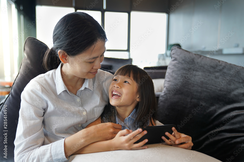 Asian mother and daughter watching cartoon on smartphone happily in the living room, quality time concept Asian mother and daughter watching cartoon on smartphone happily in the living room, quality time concept