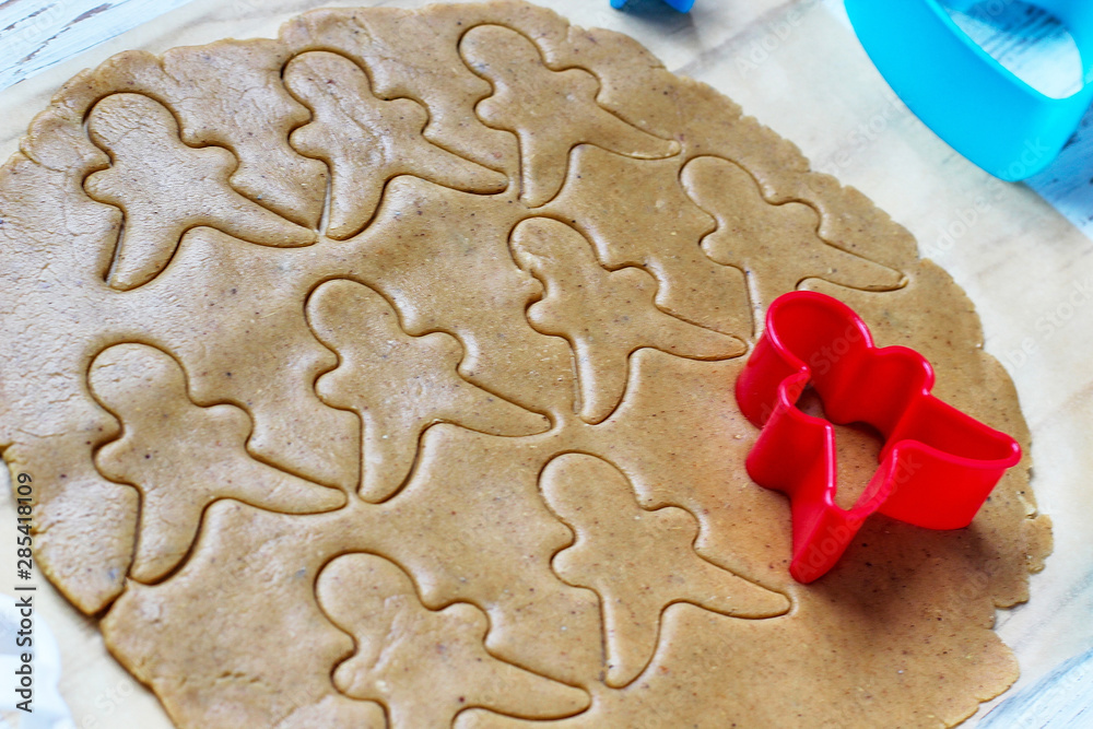 process of dealing with gingerbread man cookies,use red gingerbread man mold cutting gingerbread dough on baking paper around colorful cookie cutters on white wooden table.top view process of dealing with gingerbread man cookies,use red gingerbread man mold cutting gingerbread dough on baking paper around colorful cookie cutters on white wooden table.top view