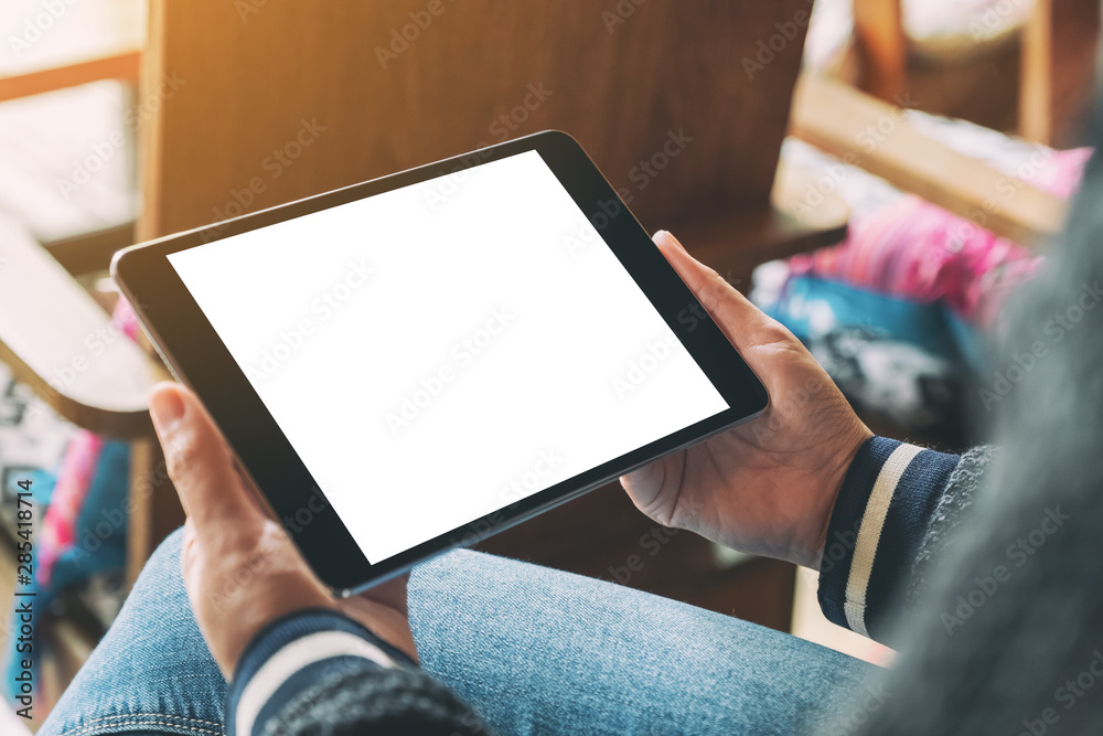 Mockup image of a woman holding black tablet with blank white desktop screen while sitting on wooden chair