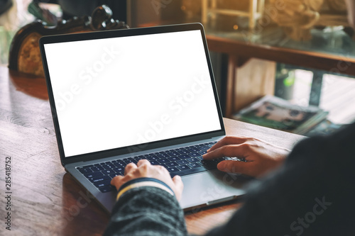 Mockup image of a woman using and typing on laptop keyboard with blank white desktop screen on wooden table