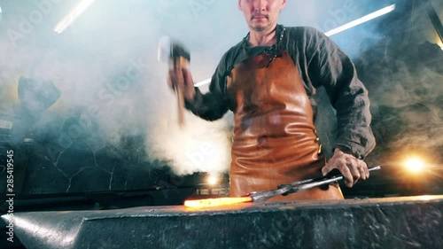 Forger hits hot knife with a hammer on anvil. Blacksmith forging iron in workshop. photo