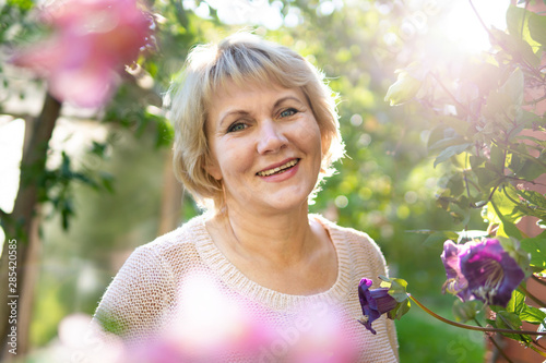 A woman in the garden chooses flowers for seedlings. A middle-aged woman looks into the camera lens. She works in villiage.