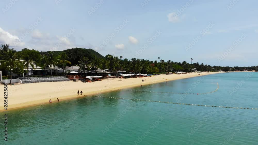 Magnificent aerial shot from above the waves of a beach with fine yellow sand lined with parasols and palm trees Magnificent aerial shot from above the waves of a beach with fine yellow sand lined with parasols and palm trees