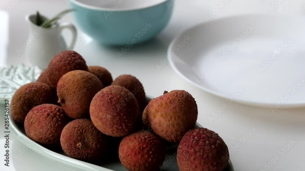 Grabbing a lychee from a pastel teal green plate, ready to peel on white ceramic plate. Grabbing a lychee from a pastel teal green plate, ready to peel on white ceramic plate.